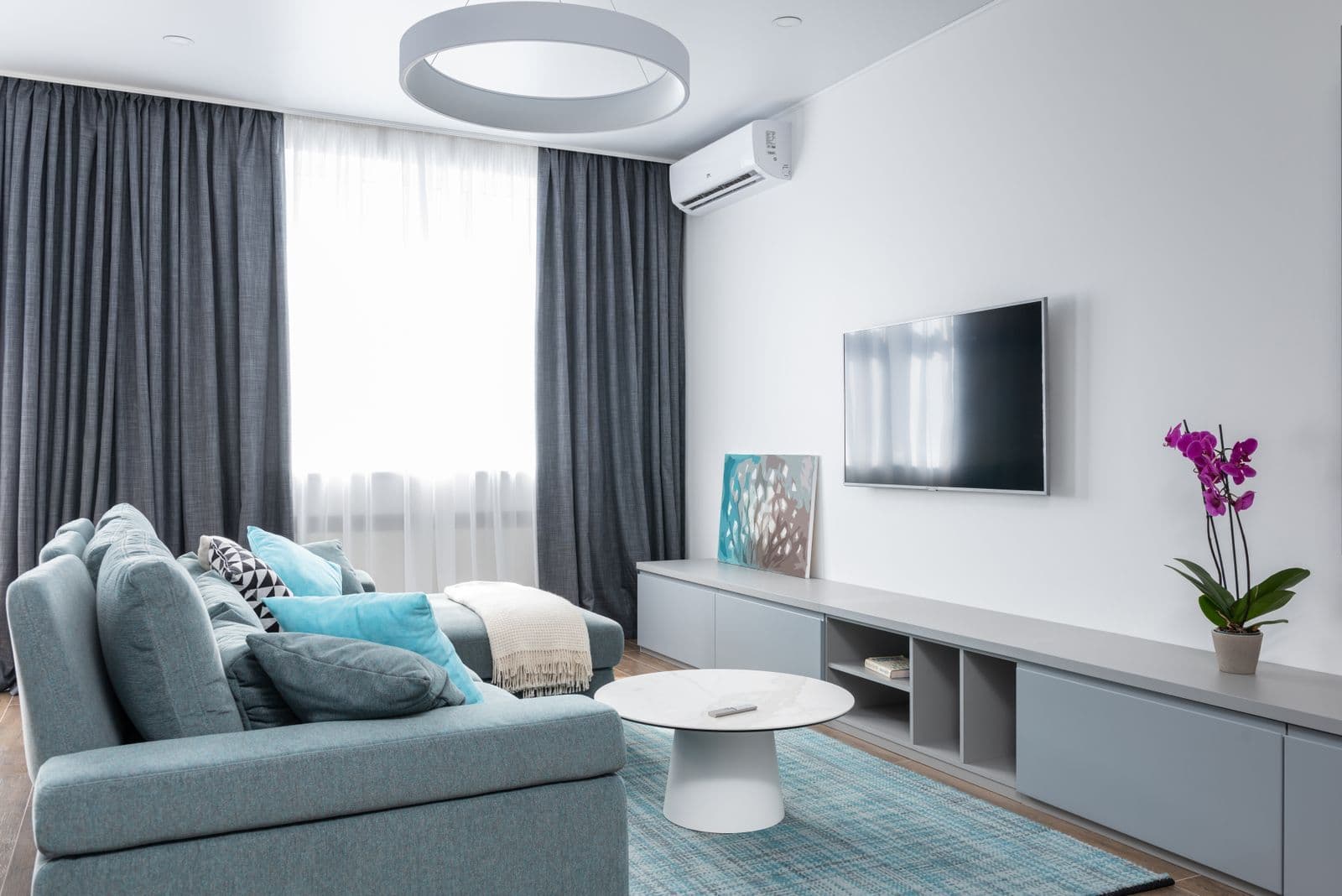 Grey living room with a TV mounted above a long console and a blue sofa