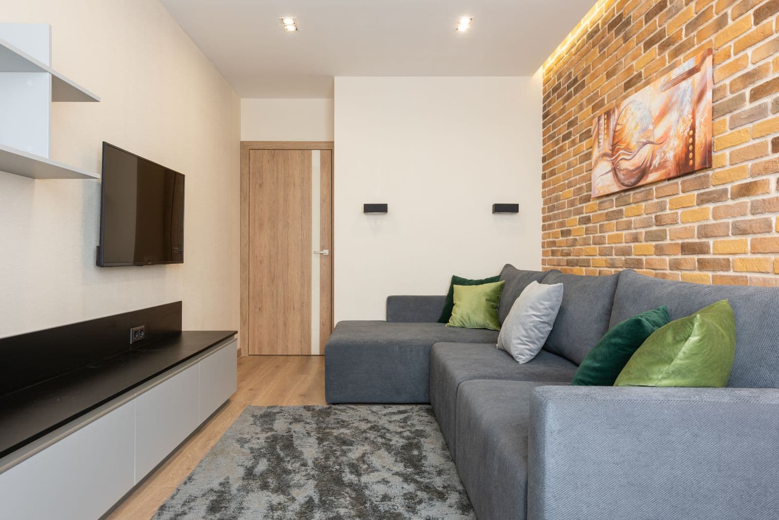 Living room with a wall-mounted TV opposite an exposed brick accent wall