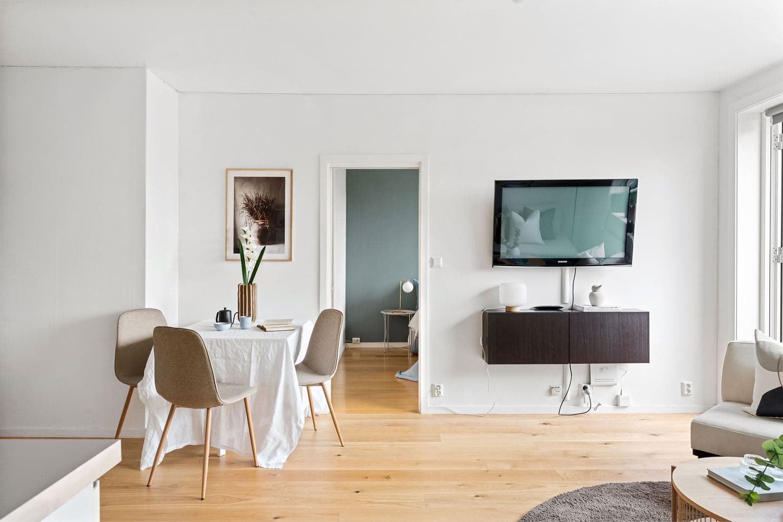 Bright, minimalist living room with a warm wood floor and a wall-mounted TV