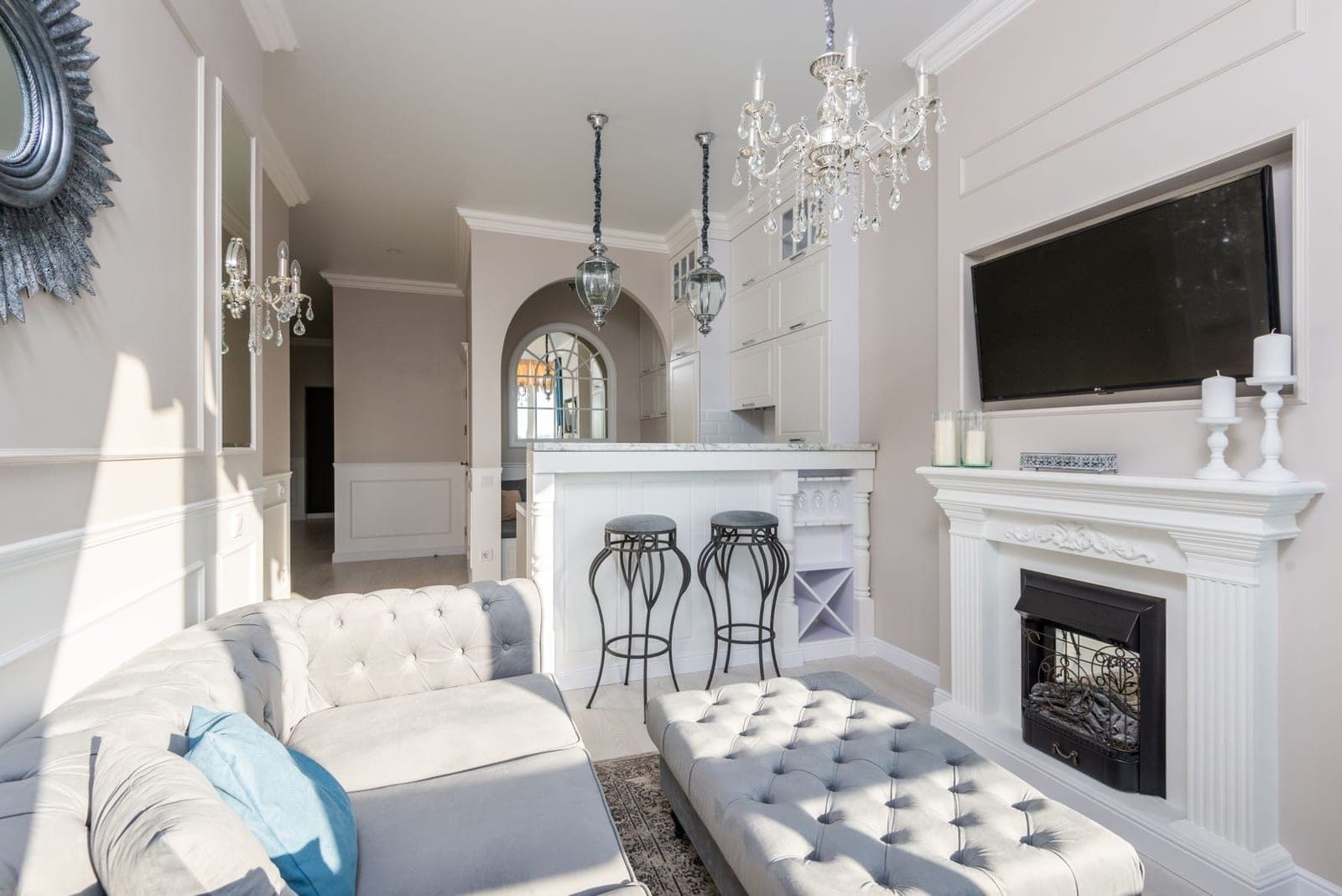 Bright white living room with a TV recessed above a classic mantel and a crystal chandelier