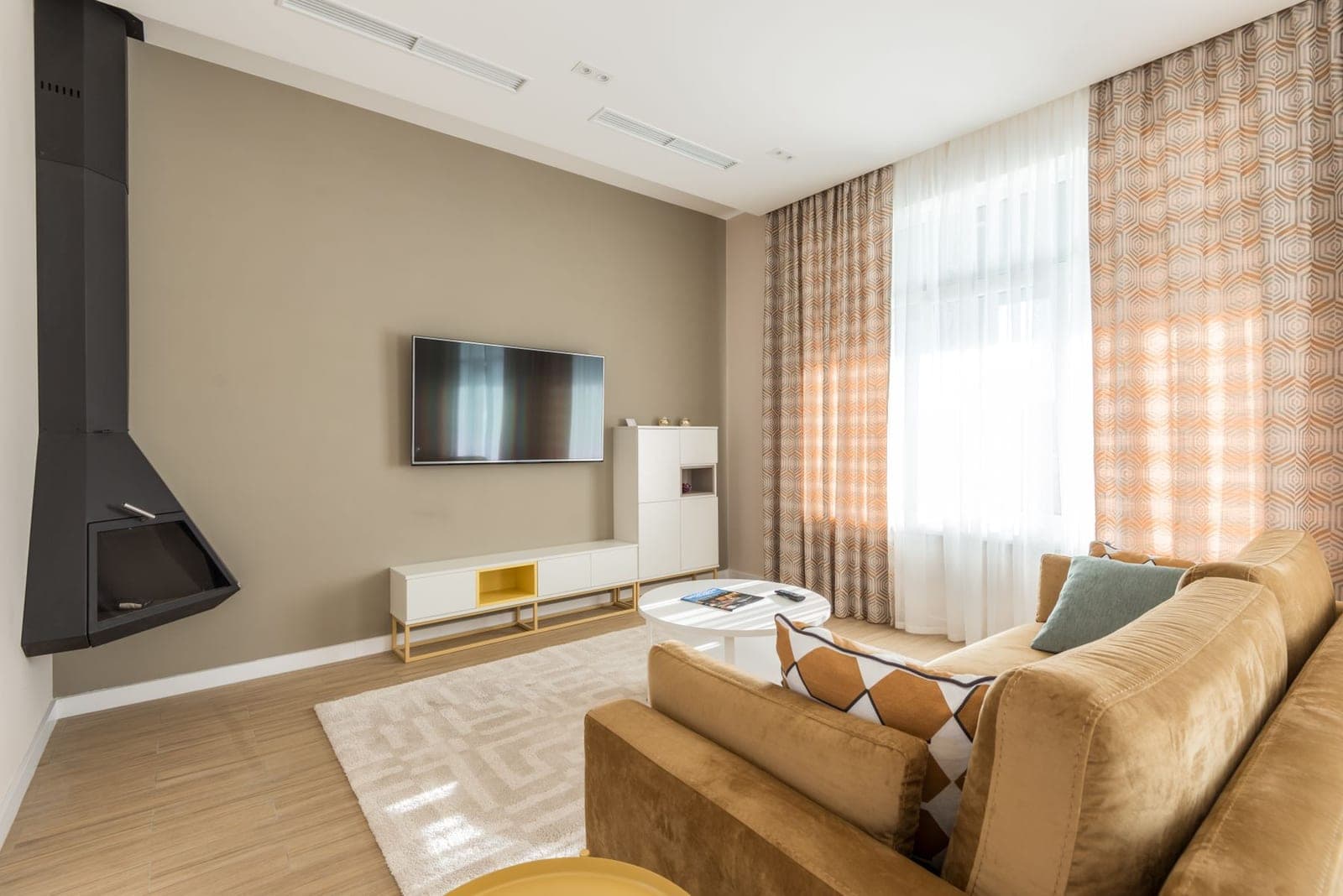 Living room with a TV mounted on a taupe wall above a white console next to a black fireplace