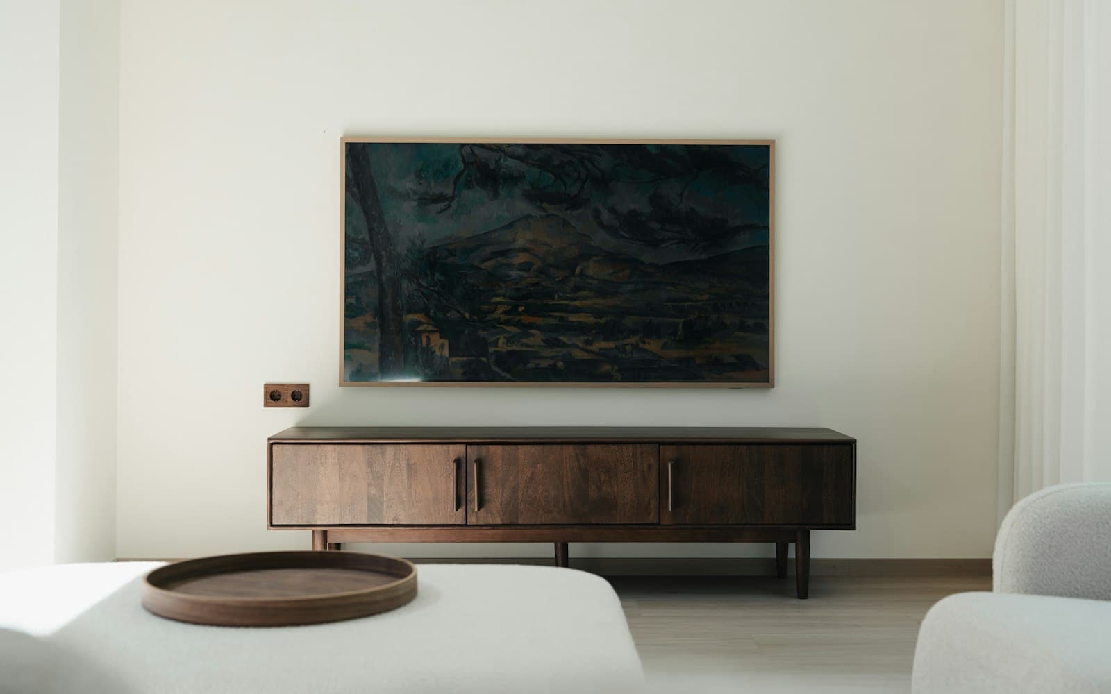 Samsung Frame TV showing a painting, mounted flush on a white wall above a walnut console