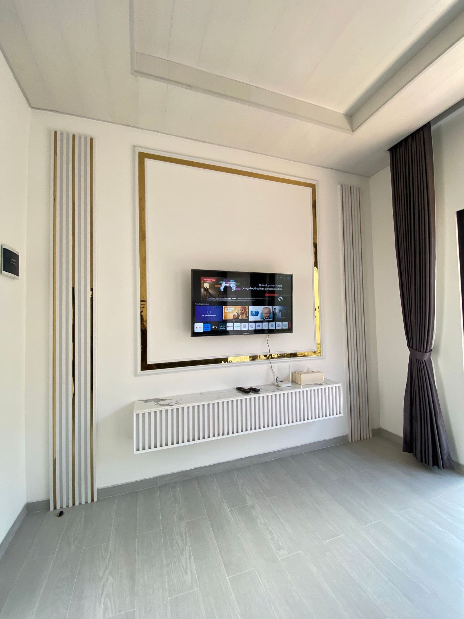Small TV centered in a white and gold trimmed wall panel above a floating console