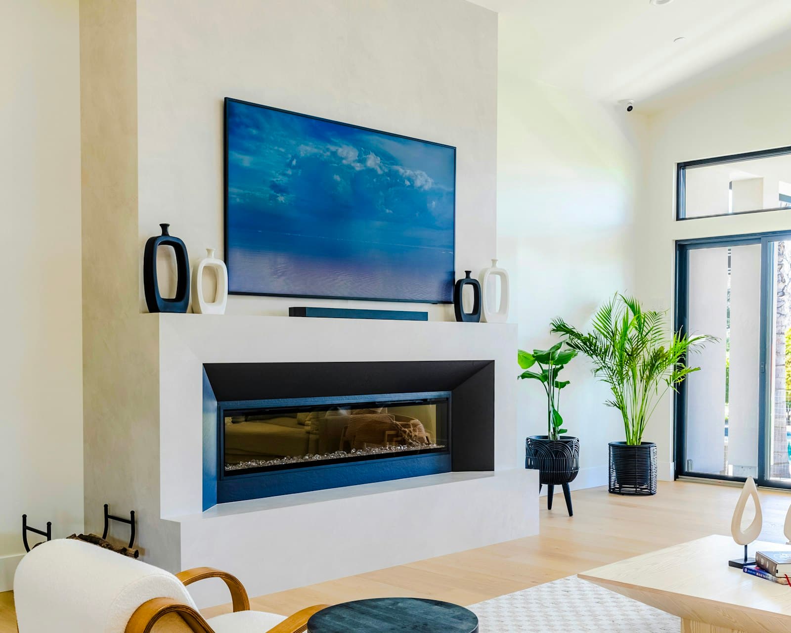 Large TV and soundbar mounted above a linear fireplace on a white plaster wall in a bright living room