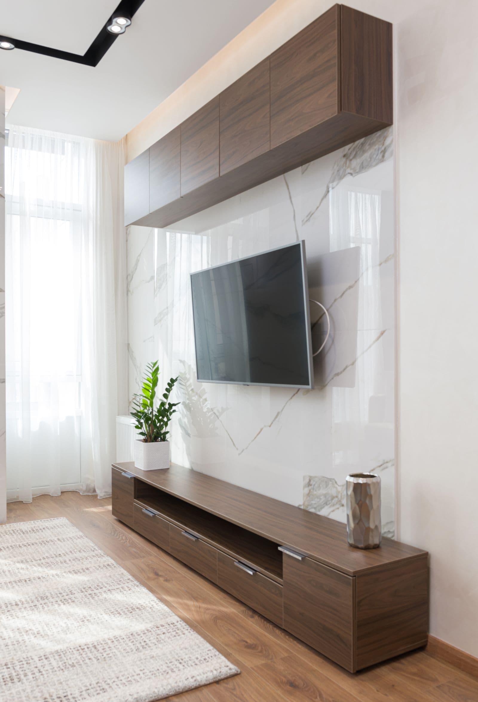 TV on a full-motion bracket angled toward the room, mounted on a marble feature wall above a walnut console