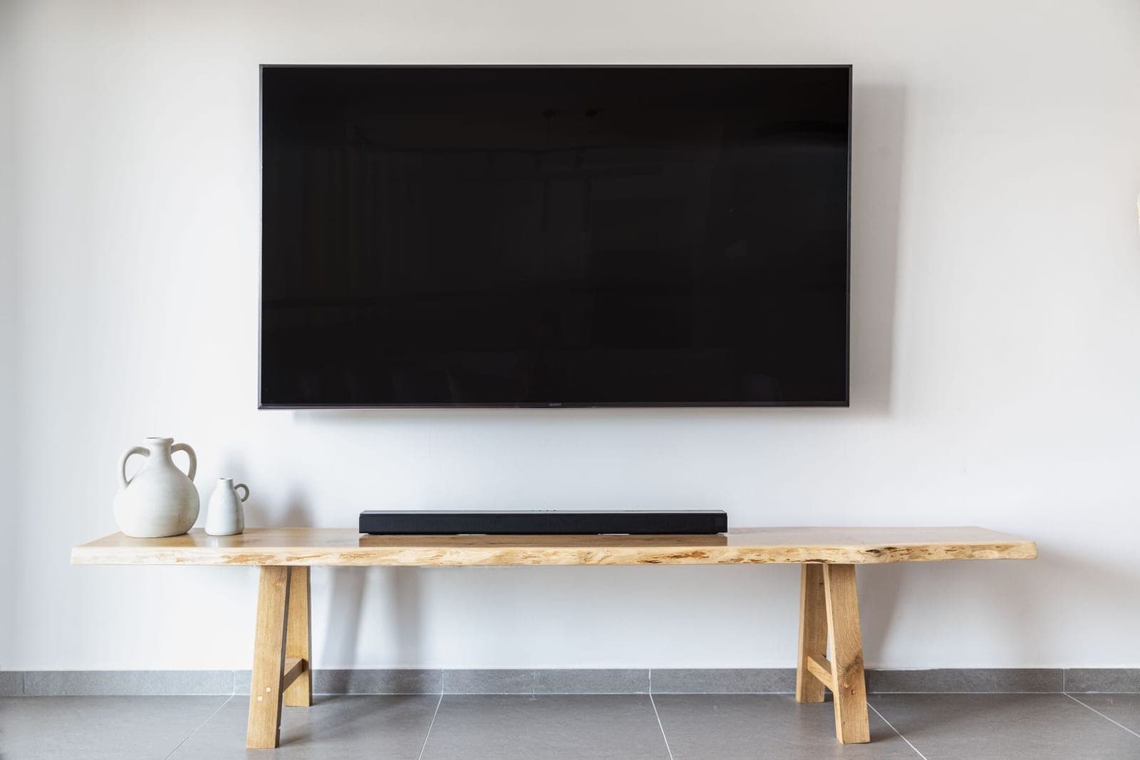 Large TV mounted on a white wall with a soundbar on a live-edge wood bench below it