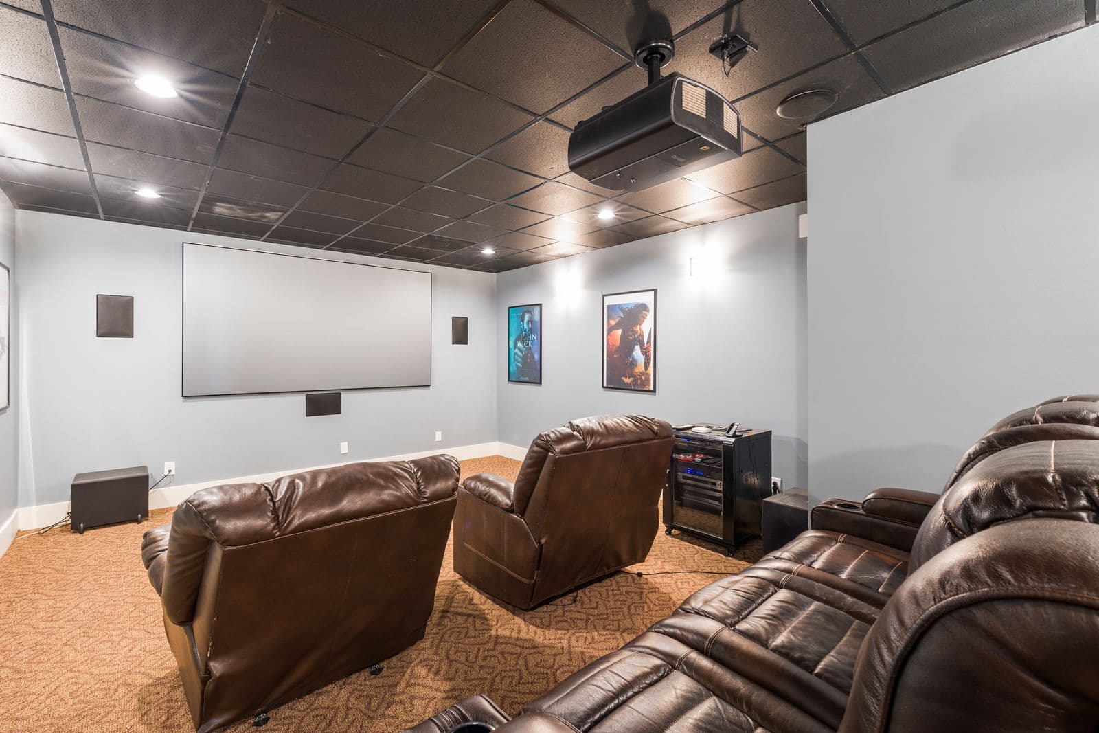 Home theater with a projector screen, in-wall speakers, and leather recliners