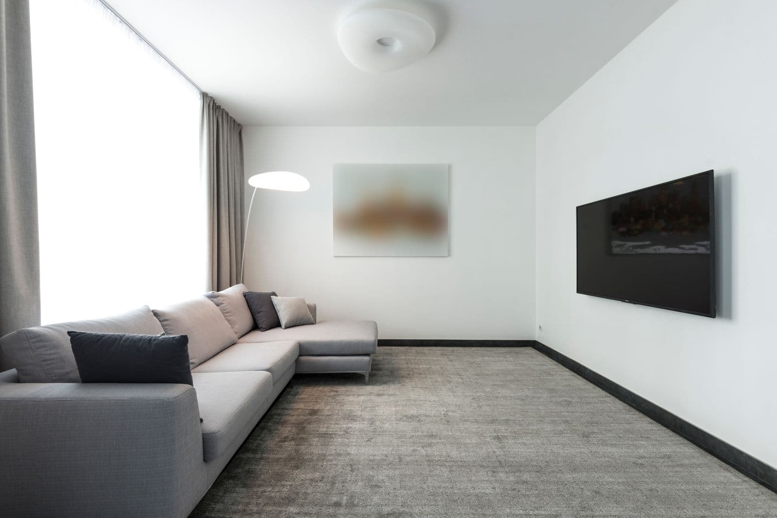 Minimal white living room with a wall-mounted TV and a grey sectional sofa